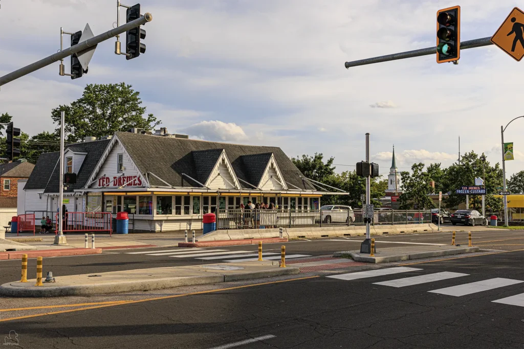 Weißer Ted-Drewes-Verkaufsbau mit roten Buchstaben und mehreren Giebeln an der Chippewa Street; davor liegen eine Fußgängerquerung, Ampeln und Absperrungen.